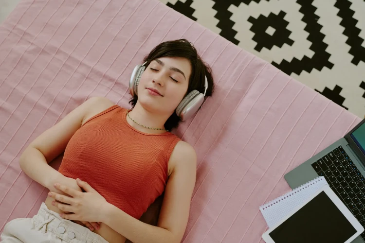 Teenage girl laying on the floor of her room while relaxing by listening to a guided hypnosis session from the AuDela mobile app